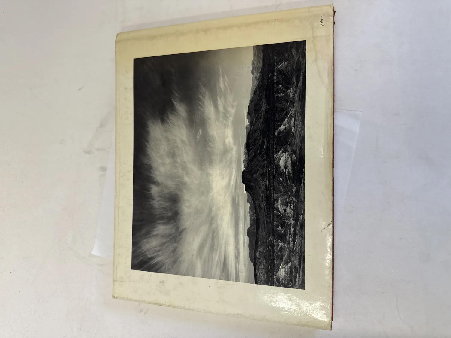 Back cover of Photographs of the Southwest by Ansel Adams showing a black-and-white landscape photograph of dramatic Southwest cliffs and sweeping cirrus clouds, dust jacket with shelf wear and toning consistent with a fifty-year-old oversize volume. Photographed at the New Mexico Literacy Project sorting desk in Albuquerque.