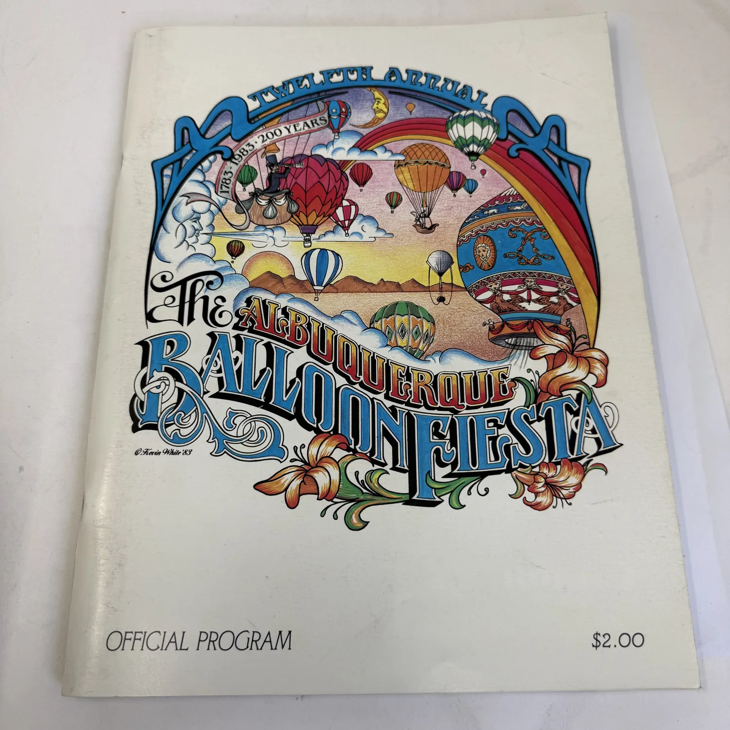 Twelfth Annual Albuquerque Balloon Fiesta Official Program 1983 — cover art by Kevin White featuring colorful hot air balloons, rainbow, and flowers, celebrating the 200th anniversary of the Montgolfier flight 1783-1983, original price $2.00. Found in an Albuquerque estate donation to the New Mexico Literacy Project.