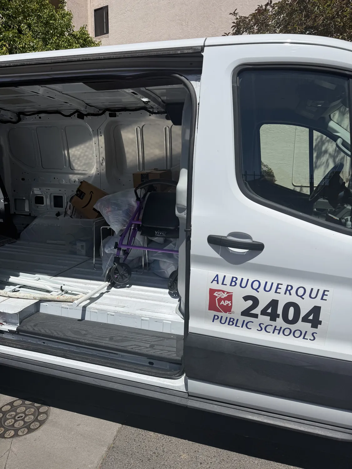 An APS Title I van with the bus number 2404 visible, parked at the NMLP warehouse on a Tuesday delivery for the McKinney-Vento program.