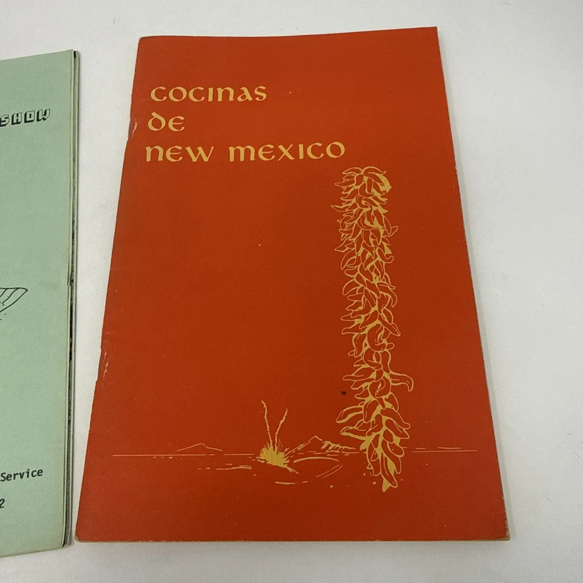 Orange Cocinas de New Mexico cover with chile ristra illustration overlapping a green New Mexico Holiday Show cover