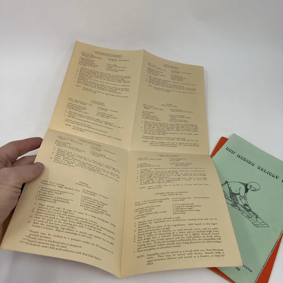 Interior recipe pages of a Cocinas de New Mexico cookbook held open by hand, showing mid-century typewriter-typeface recipes for traditional dishes