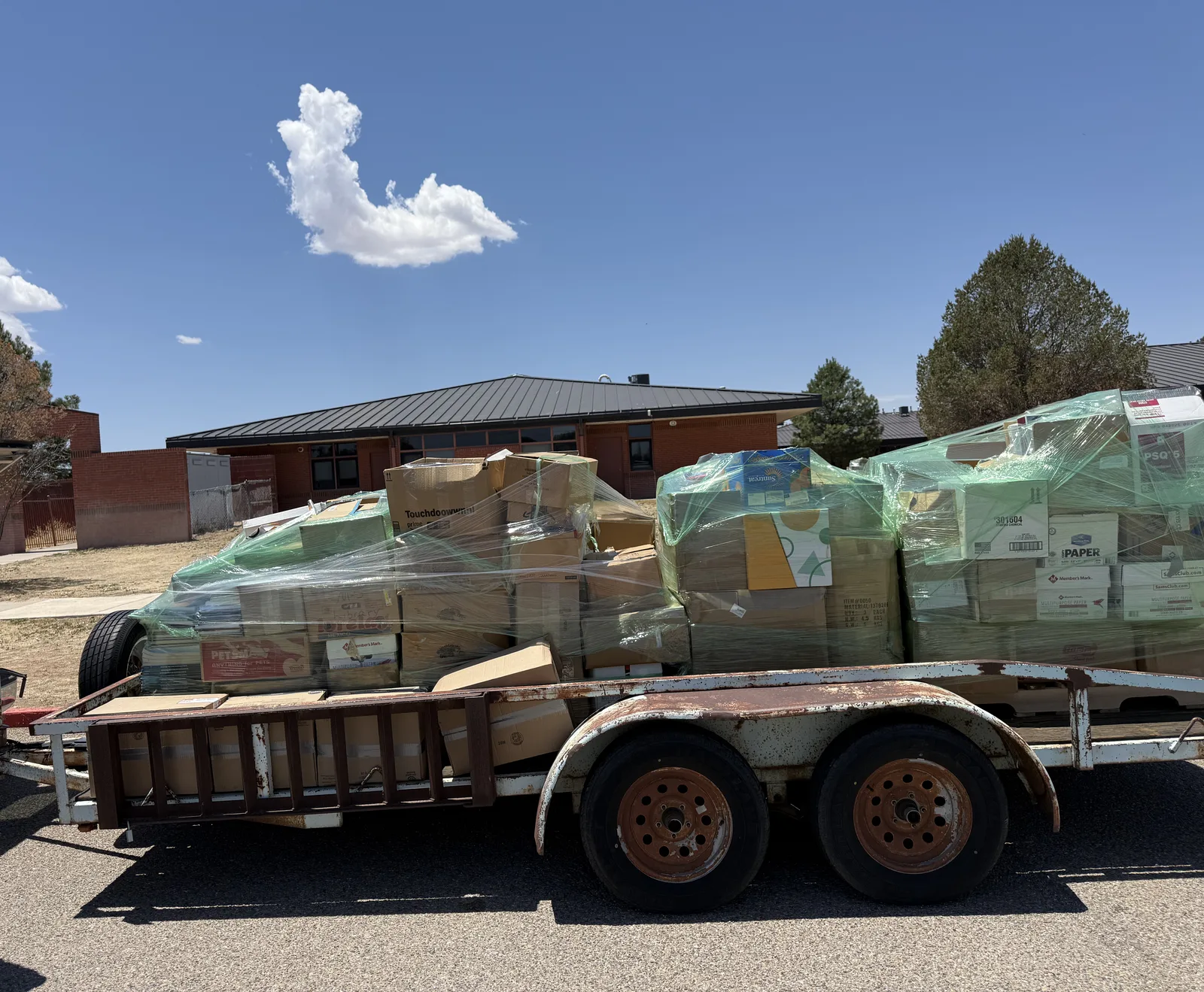 Tandem-axle utility trailer carrying shrink-wrapped pallet stacks of boxed donated books under a blue Albuquerque sky