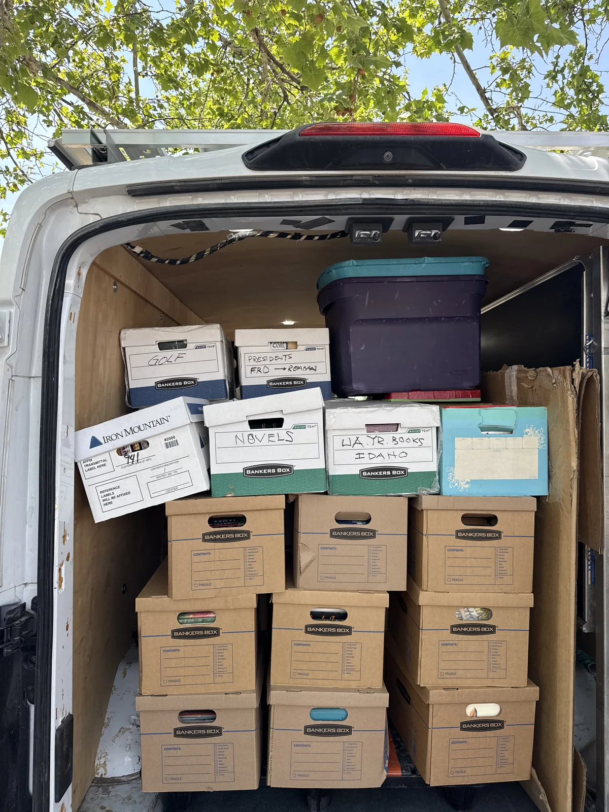 Rear doors open on the New Mexico Literacy Project cargo van, the bay stacked with labeled banker boxes of donated books and a storage tote