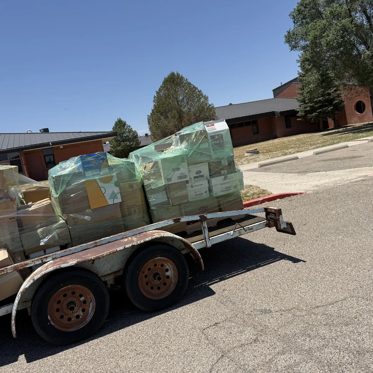 A loaded utility trailer of shrink-wrapped book pallets hitched and ready to haul out of an Estancia school parking lot during a free New Mexico Literacy Project school book-removal pickup. June 2026.