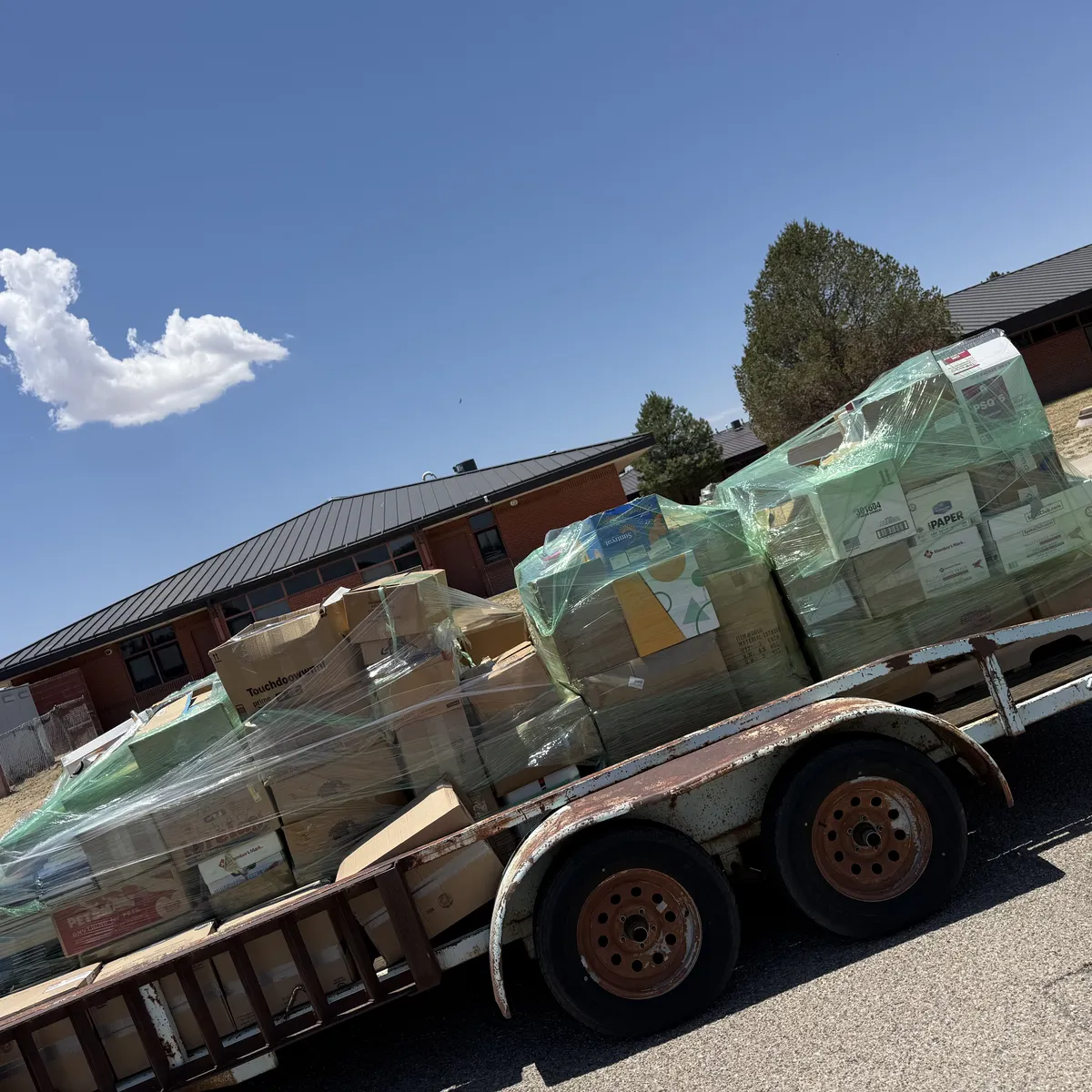 A utility trailer parked outside an Estancia, New Mexico school, loaded with shrink-wrapped pallets of boxed excess books bound for hand-sorting at the New Mexico Literacy Project warehouse in Albuquerque. June 2026.