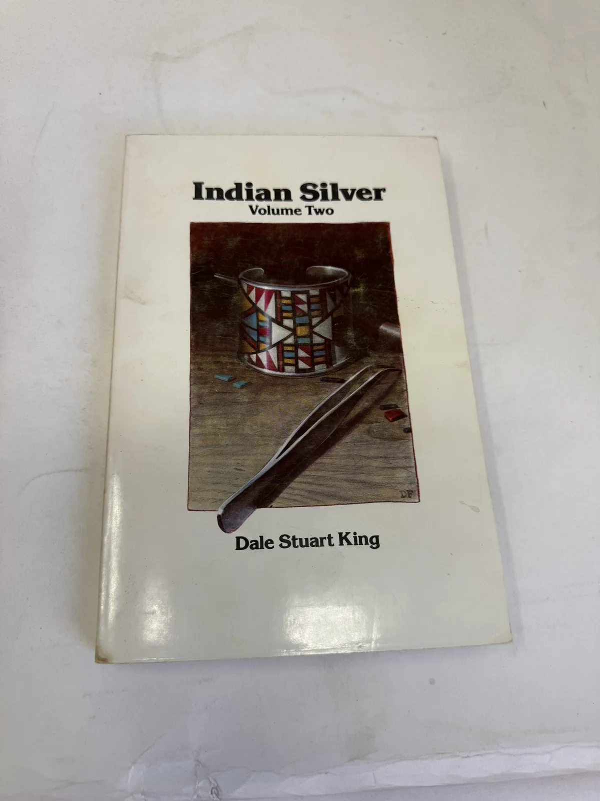 Cover of Indian Silver Volume Two by Dale Stuart King showing a silver concho and stamped bracelet on a dark ground, photographed at New Mexico Literacy Project