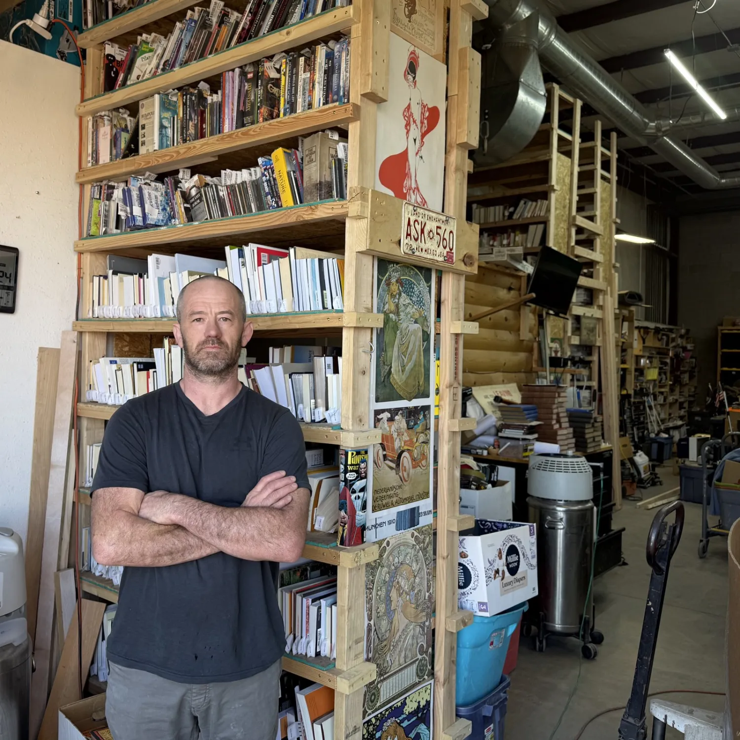Josh Eldred at the New Mexico Literacy Project warehouse, standing in front of the sorted-book wall where every donation gets hand-evaluated before routing