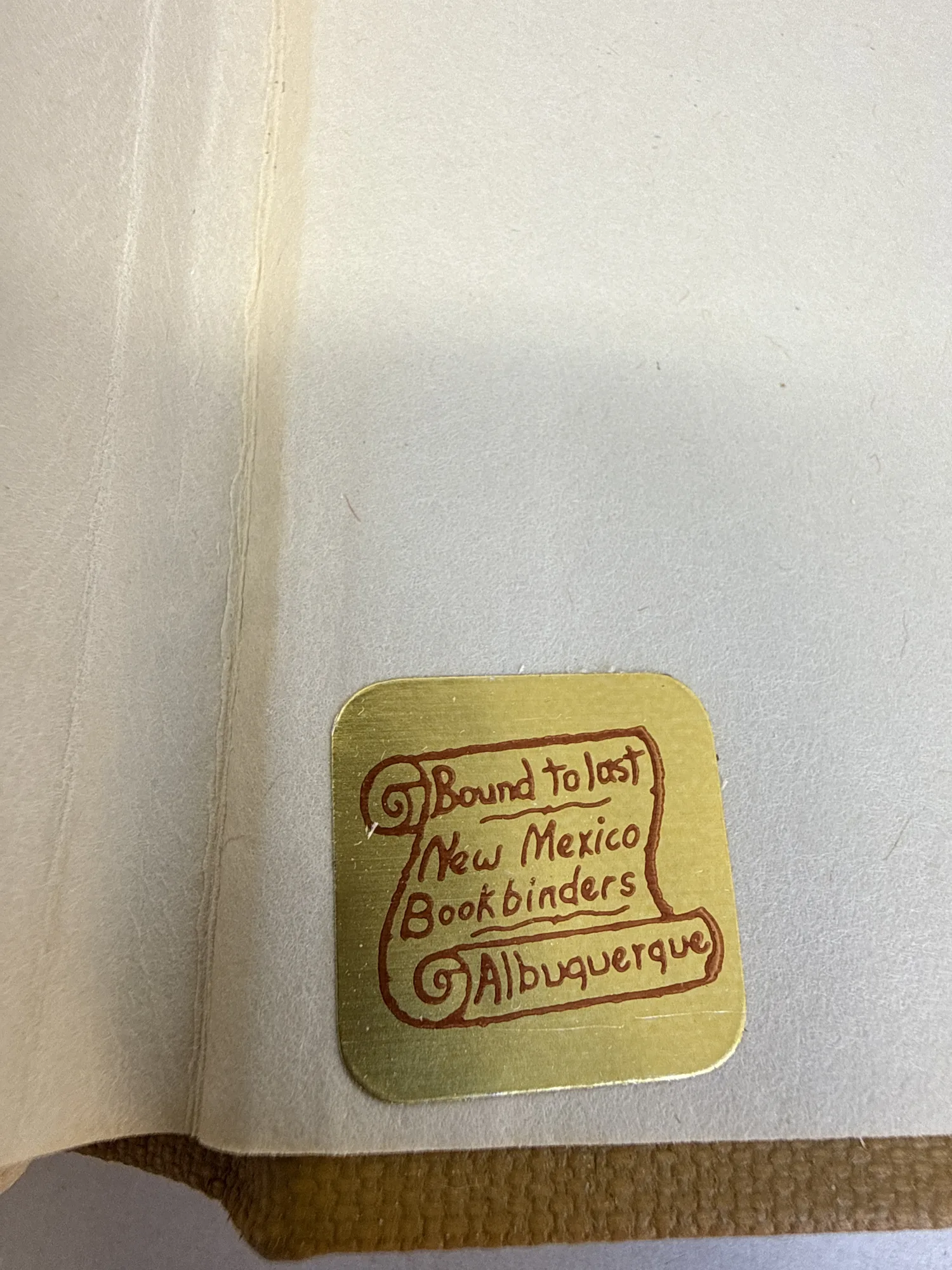 Gold foil sticker inside cover reading Bound to Last New Mexico Bookbinders Albuquerque, showing local Albuquerque bindery provenance. Photographed at the New Mexico Literacy Project sorting desk in Albuquerque.