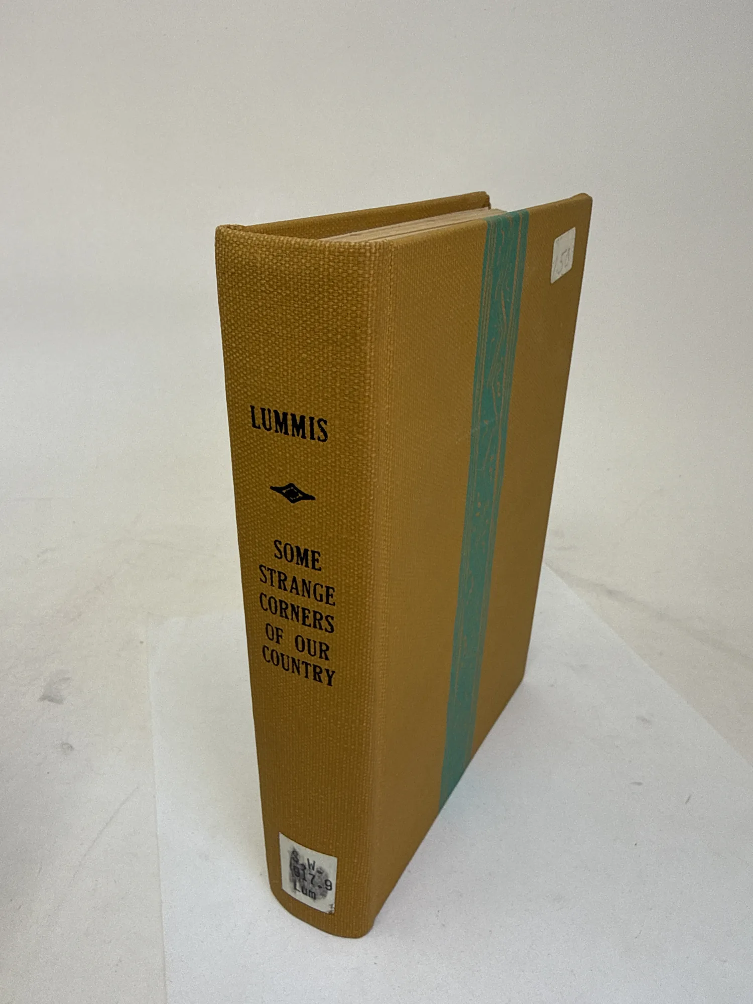 Spine of Some Strange Corners of Our Country by Charles F. Lummis showing gold-tan cloth library rebinding with turquoise band by New Mexico Bookbinders Albuquerque. Photographed at the New Mexico Literacy Project sorting desk in Albuquerque.