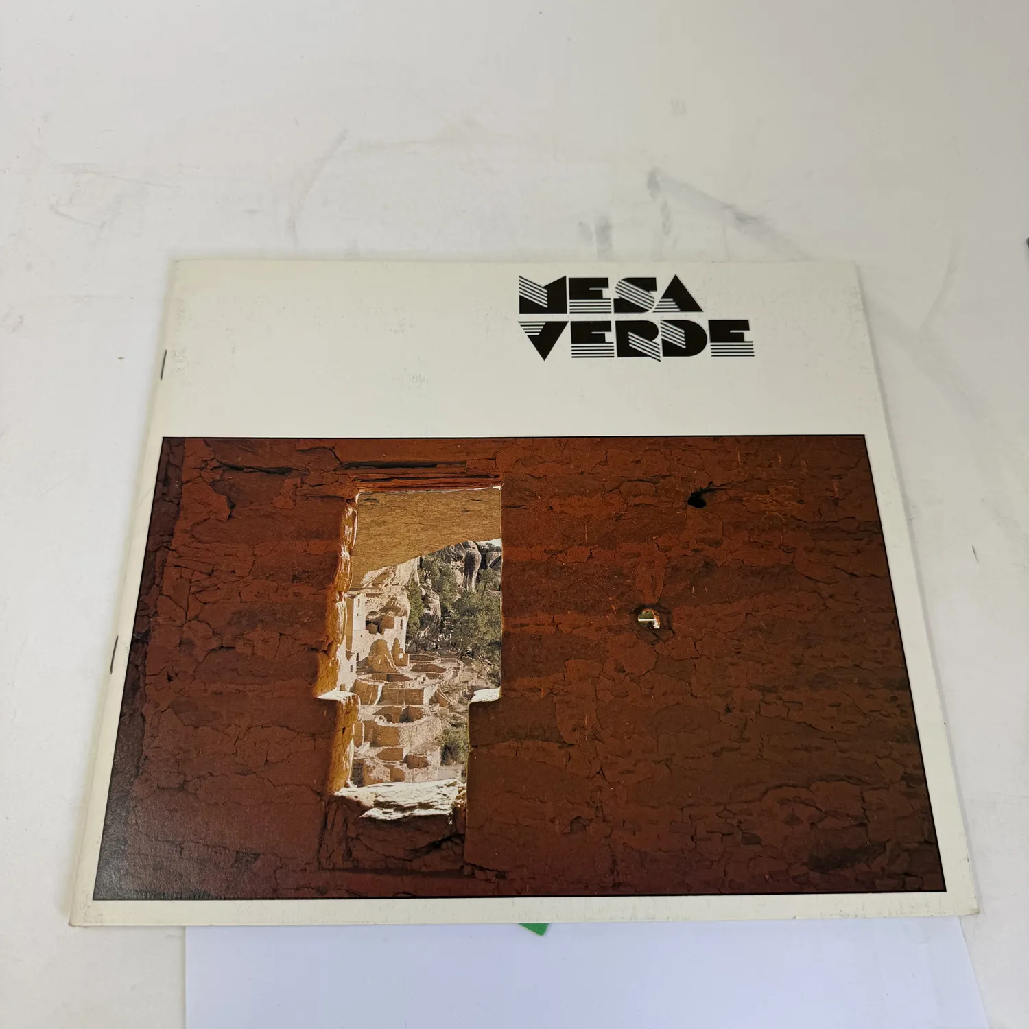 Vintage Mesa Verde National Park photo guide book with stylized 1970s typography and a photograph of Ancestral Puebloan cliff dwellings seen through a stone doorway in red sandstone. Southwest collectible ephemera found in an Albuquerque estate donation to the New Mexico Literacy Project.