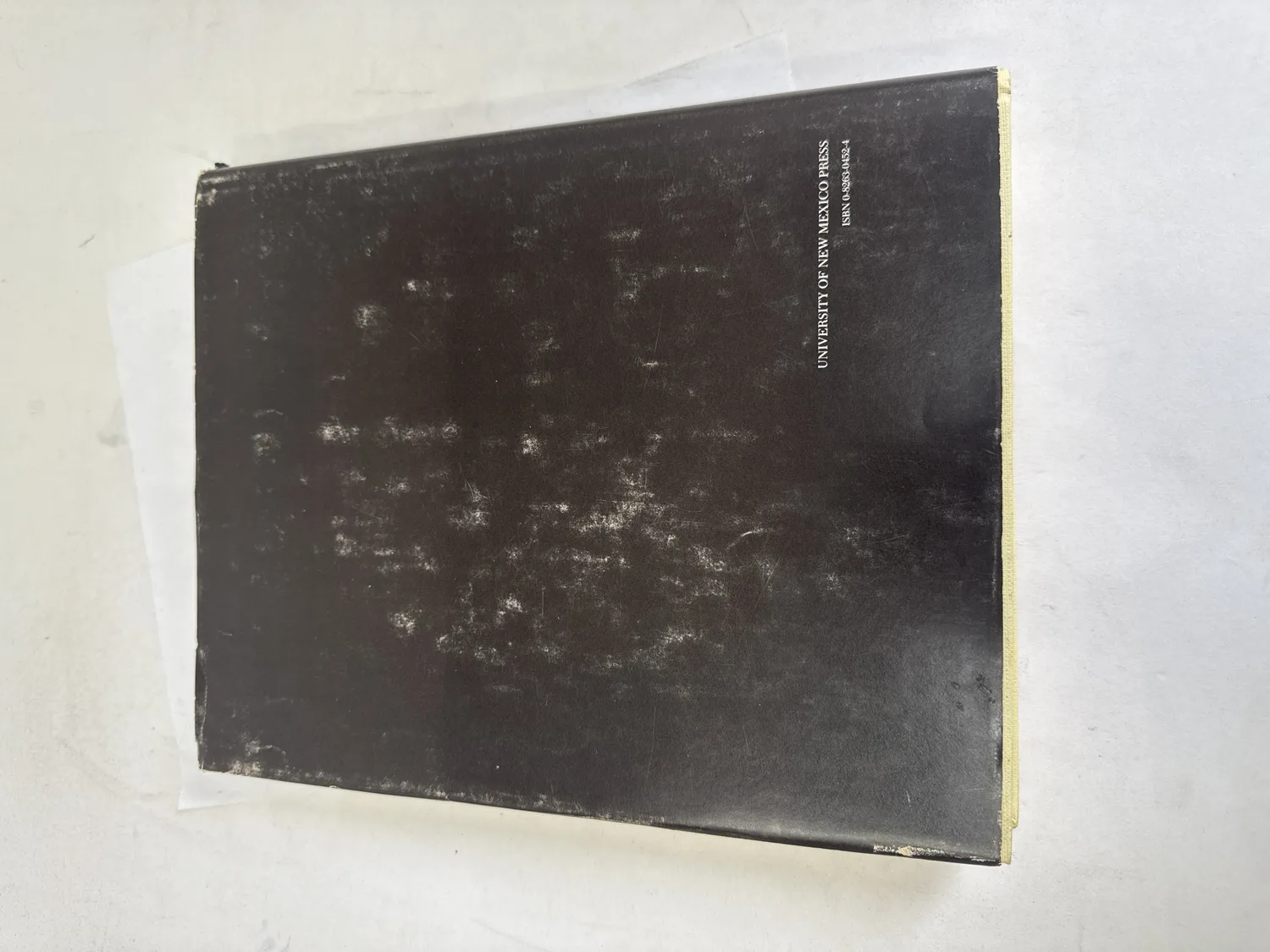 Back cover of Mimbres Painted Pottery by J.J. Brody, 1977 first edition, plain black with University of New Mexico Press imprint and ISBN, showing significant wear and surface scuffing from decades of use. Photographed at the New Mexico Literacy Project sorting desk in Albuquerque.