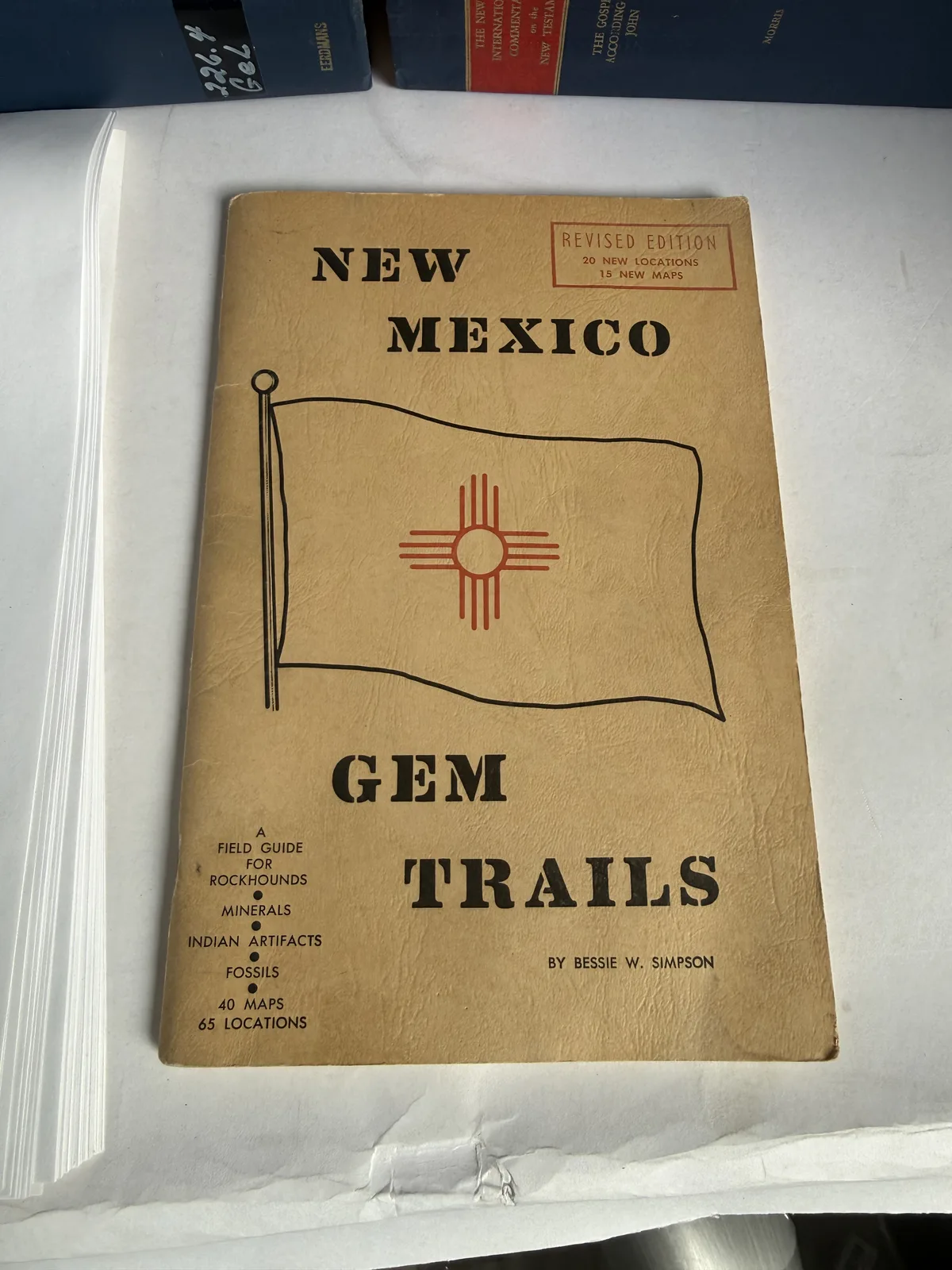 Tan cover of New Mexico Gem Trails by Bessie W Simpson, a field guide for gem and mineral collectors, with the New Mexico Zia flag, photographed at New Mexico Literacy Project