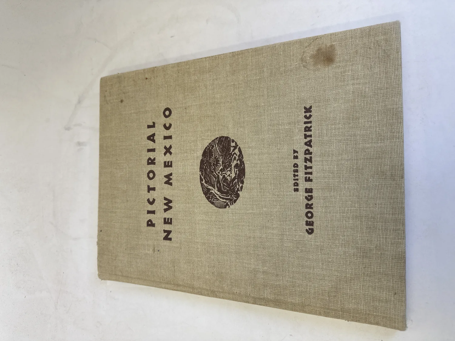 Cloth-bound cover of Pictorial New Mexico edited by George Fitzpatrick, 1949 first printing, with woodcut landscape vignette on tan buckram binding. Photographed at the New Mexico Literacy Project sorting desk in Albuquerque.