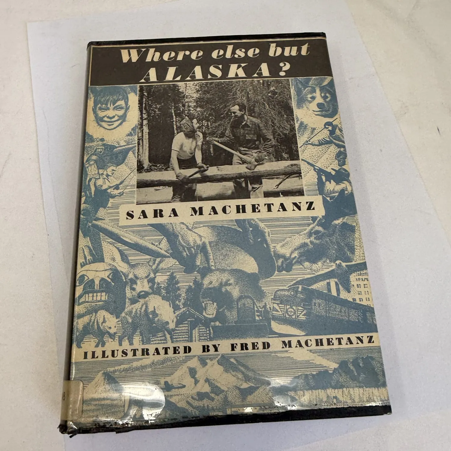 Front cover with dust jacket of Where Else but Alaska by Sara Machetanz illustrated by Fred Machetanz, Charles Scribner's Sons 1954, showing blue-toned collage artwork of Alaskan life including moose, sled dogs, bush pilot, locomotive, wildlife, and a central photograph of the Machetanzes working at a log in the wilderness. Ex-library copy found in a New Mexico estate cleanout by the New Mexico Literacy Project.