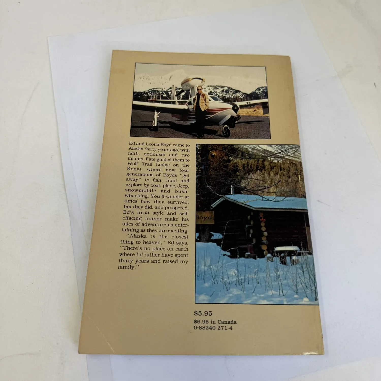 Back cover of Wolf Trail Lodge by Edward M. Boyd showing two photographs: Ed Boyd standing by his small plane on an Alaskan mountain airstrip with mountains behind, and the Boyds lodge building in winter snow with hand-painted Boyds sign. Text describing Ed and Leona coming to Alaska thirty years ago with faith optimism and two infants. $5.95 US $6.95 Canada, ISBN 0-88240-271-4.